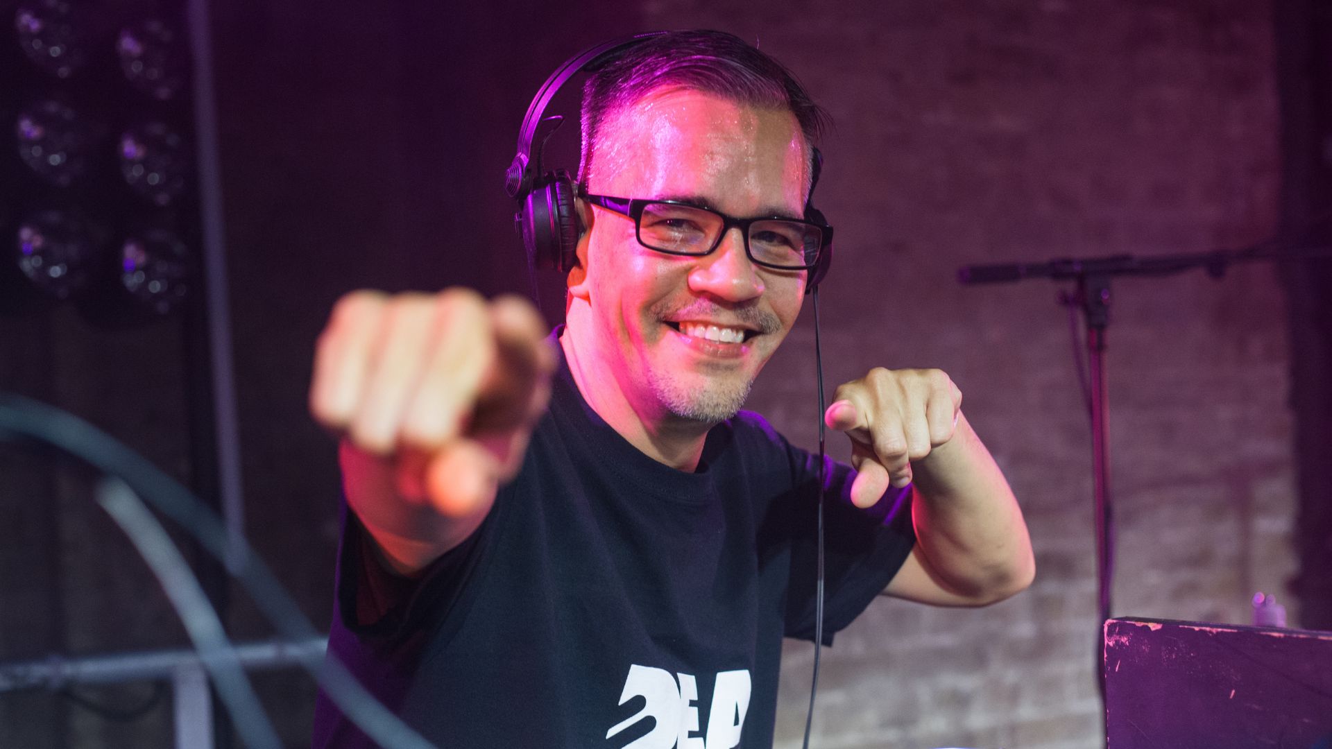 A photo of Troi Lee MBE, Deaf Rave organiser, pointing to the camera and smiling.