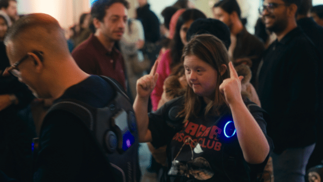 A photo of a young woman dancing in a room full of people.