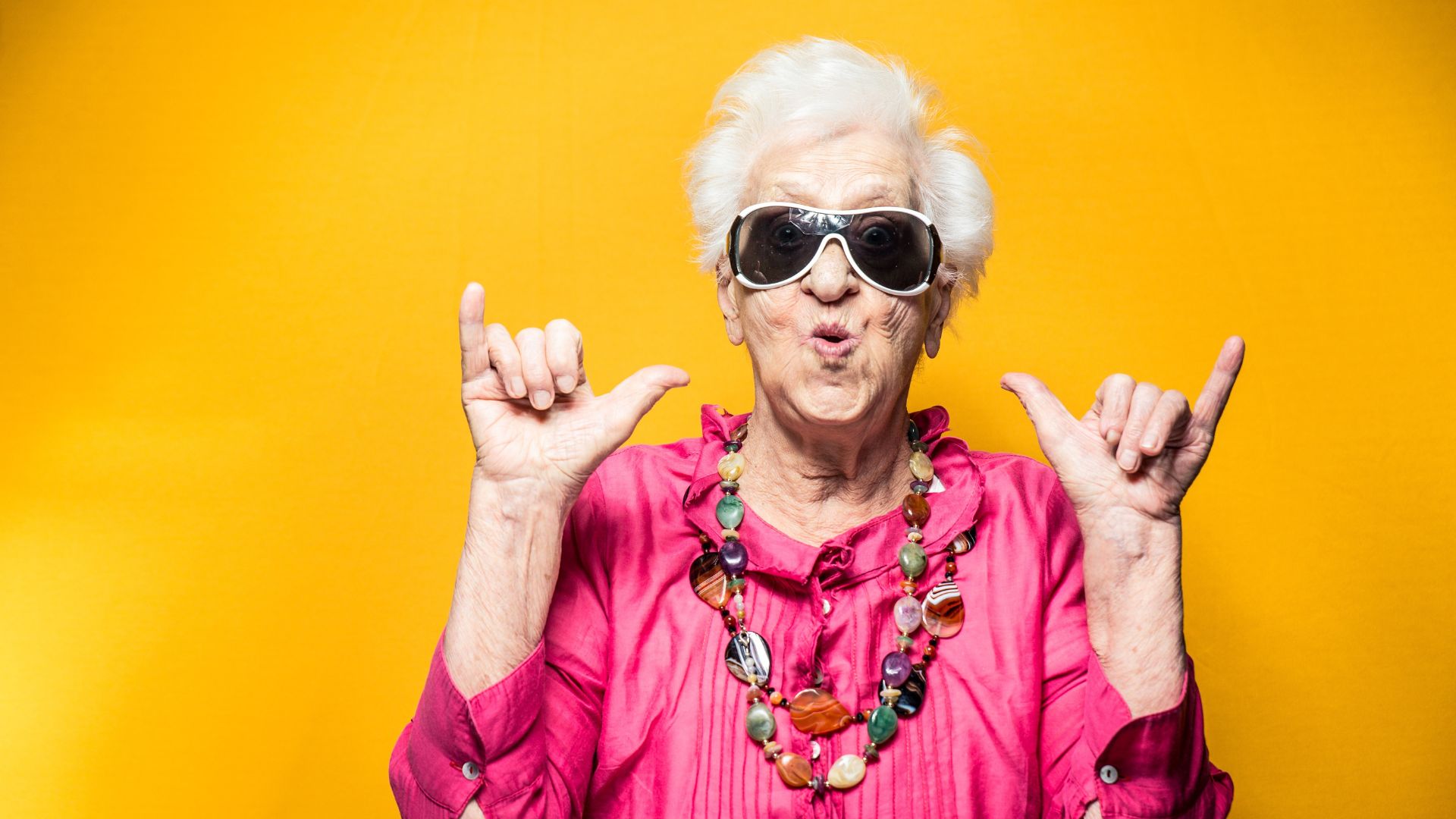 A picture of an old lady wearing sunglasses and a funky necklace. She is doing a