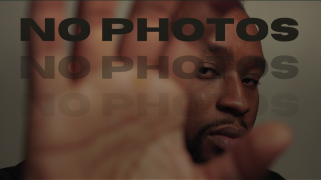 Image of a person holding their hand up to the camera to hide their face. Behind their hand, the person's face can be seen, looking into the camera. The words 'No Photos' are repeated and overlayed over the image, fading with each line over the image.