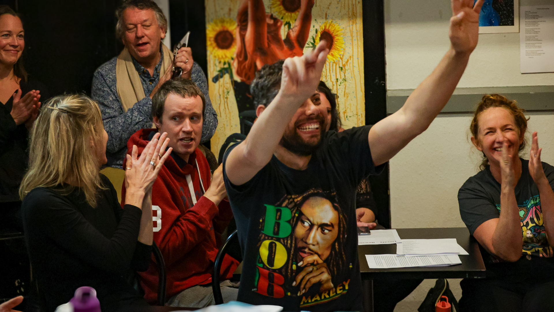 Image of audience members clapping. One audience member holds their hands in the air.