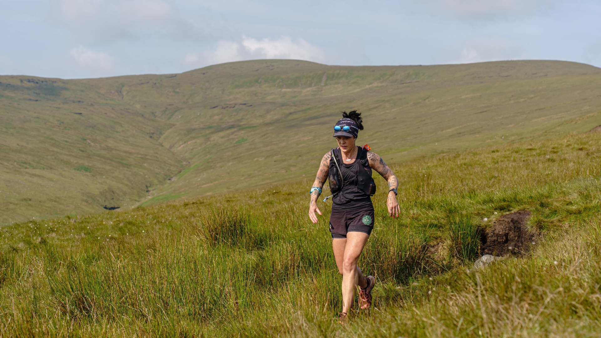 A photo of Allie Bailey running down a hill. She has running gear on, and the landscape is grassy with a blue sky.