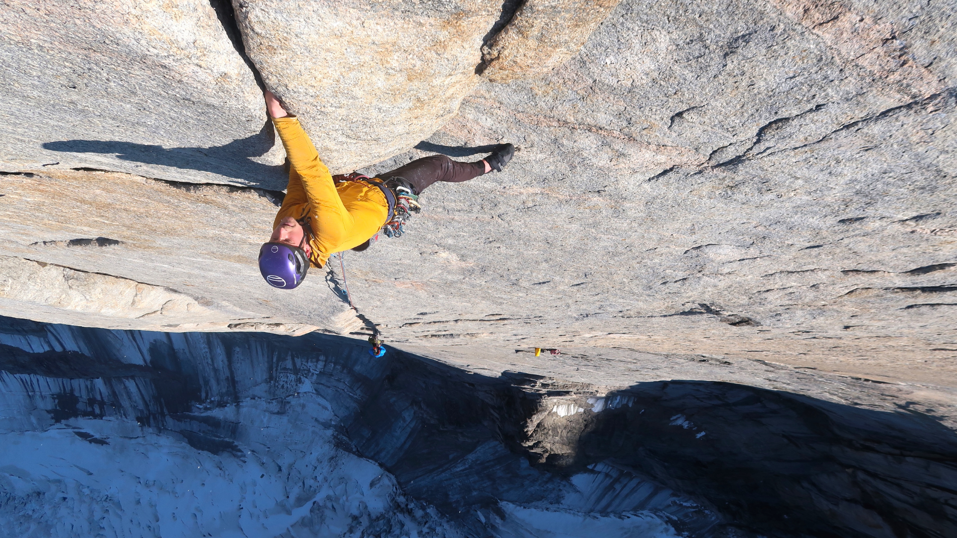 Image of a person rock climbing. They are wearing a purple helmet and yellow top.